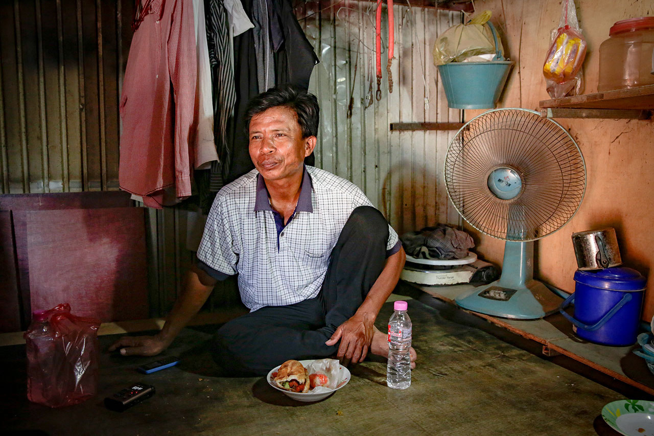 Lounh Bunthoen sitting on the floor in his hut, eating a meal.